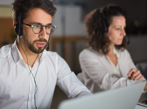 Front view of call center operator communicating with client. Confident young man in eyeglasses looking at screen of laptop and talking. Call center concept