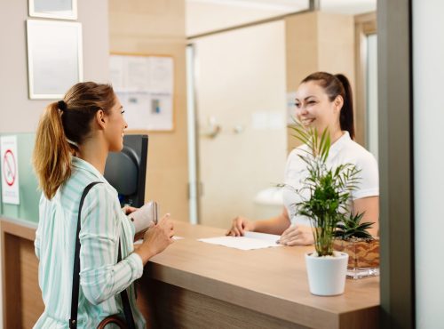 Young happy woman checking in health spa and communicating with a receptionist.